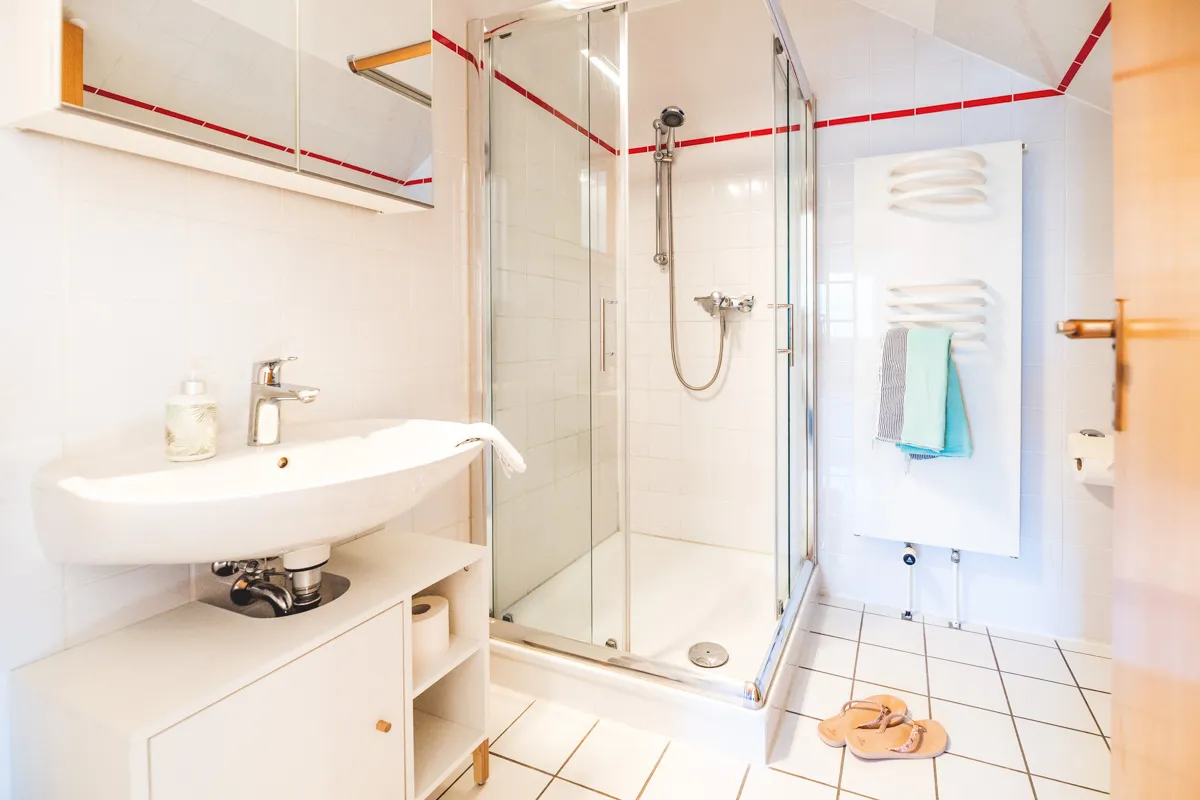 Badezimmer mit Eckdusche hinter Glastüren, Waschbecken mit Unterschrank und Handtuchheizkörper