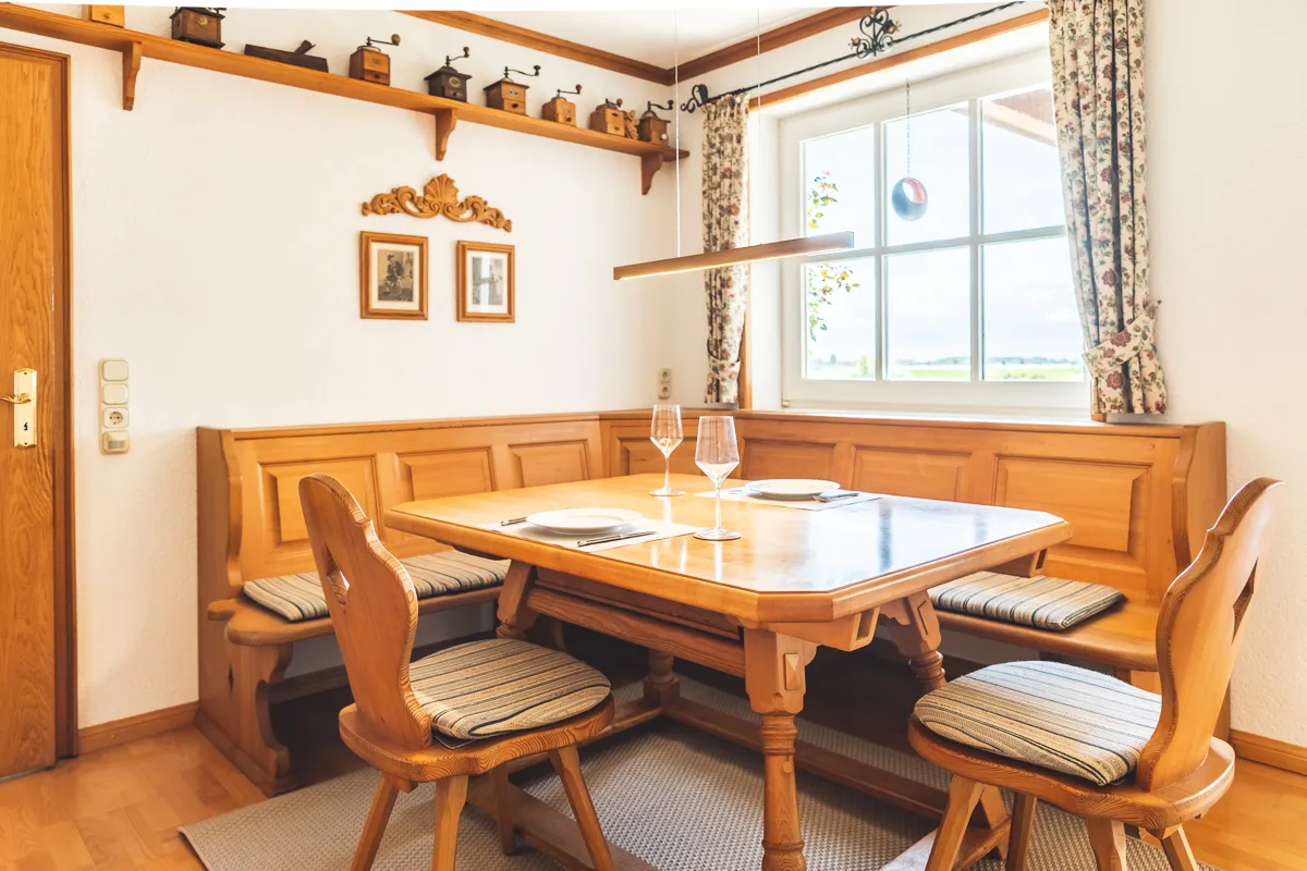 Gedeckte Eckbank aus Holz am Fenster, darüber ein Regal mit alten Kaffeemühlen