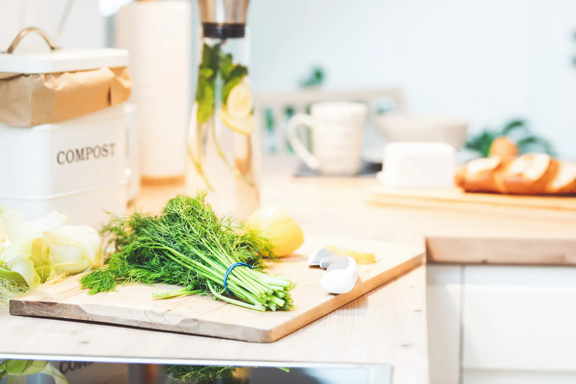 Küchenarbeitsplatte mit Schneidebrett, Dill, Fenchel und einer Zitrone, daneben Kompostbehälter und Küchenrolle