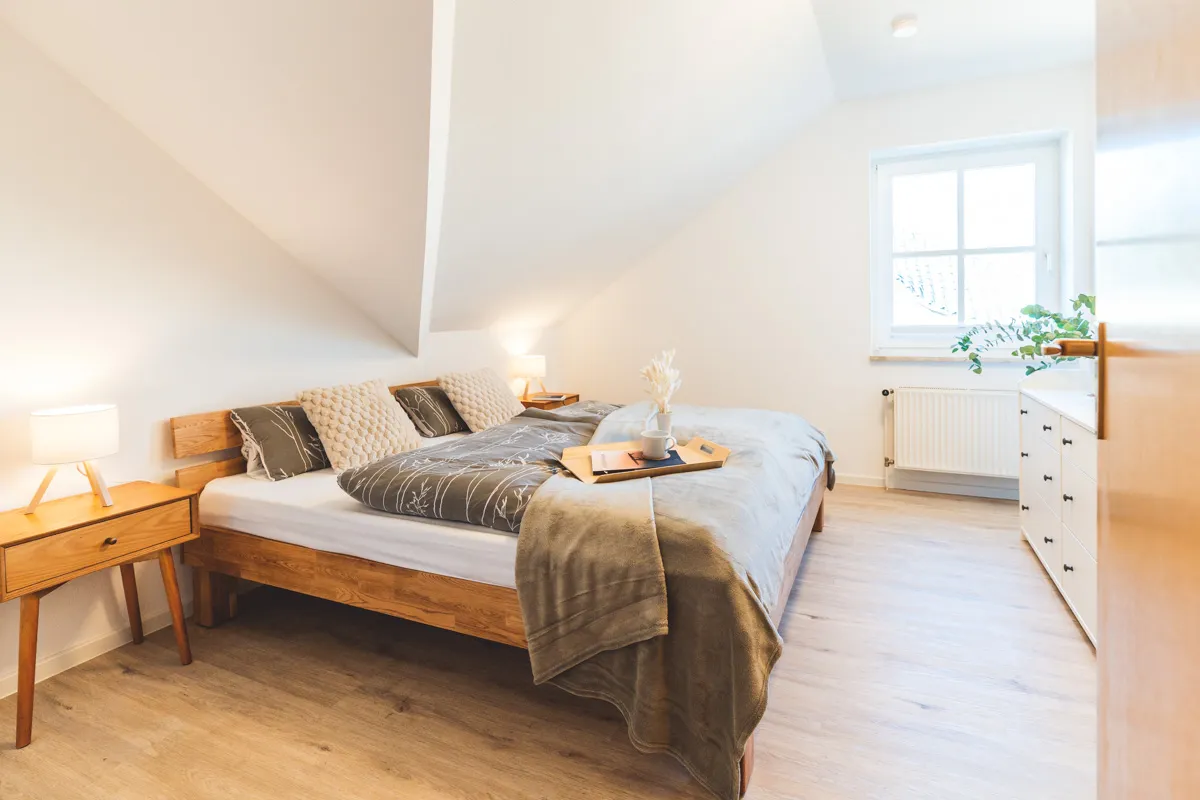 Schlafzimmer mit Doppelbett aus Eiche unter der Dachschräge, zwei Nachttische mit Leselampen, am Fußende ein Tablett mit Kaffeetasse
