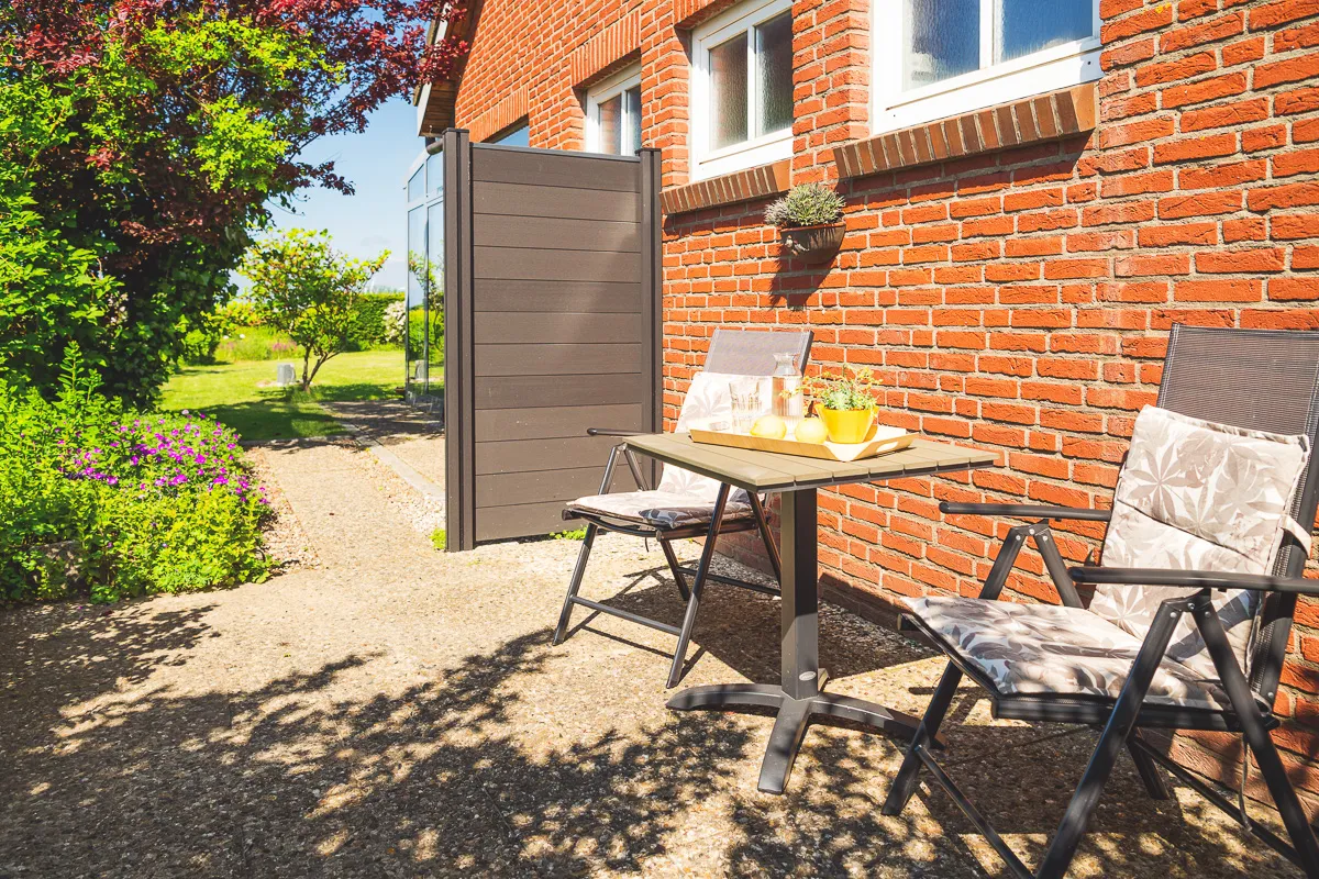 Dieselbe Außenterrasse aus der anderen Richtung, links ein Sichtschutzelement, dahinter der Blick in den Garten