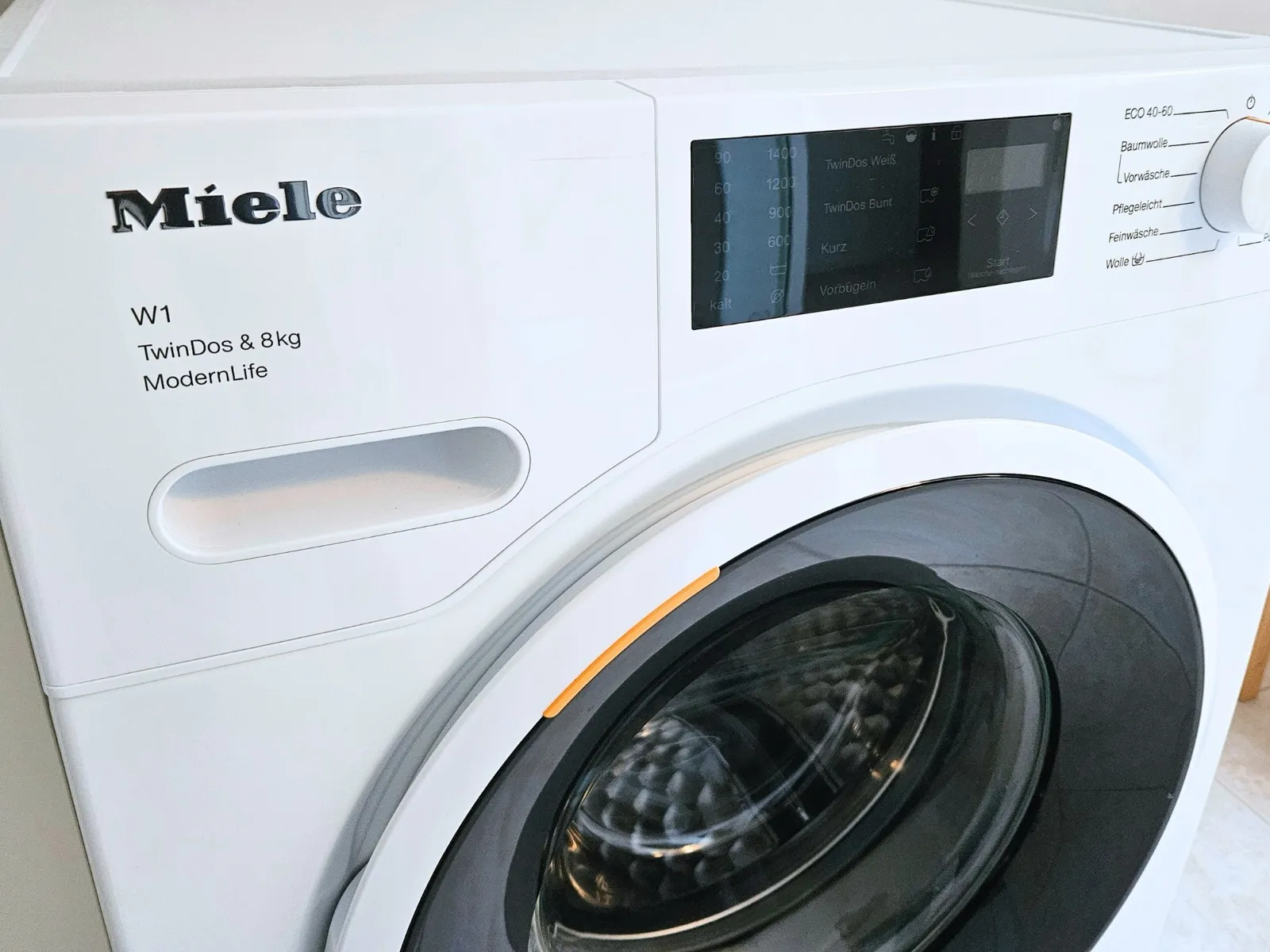 Weiße Miele-Waschmaschine W1 TwinDos mit 8 kg Fassungsvermögen im Anschnitt, Bullauge und Bedienfeld mit Programmwahl gut sichtbar